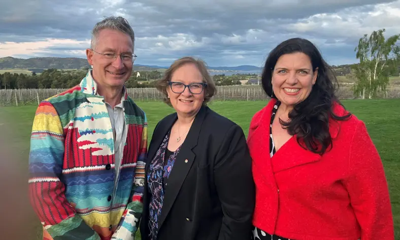 Three people standing together outside and smiling at the camera