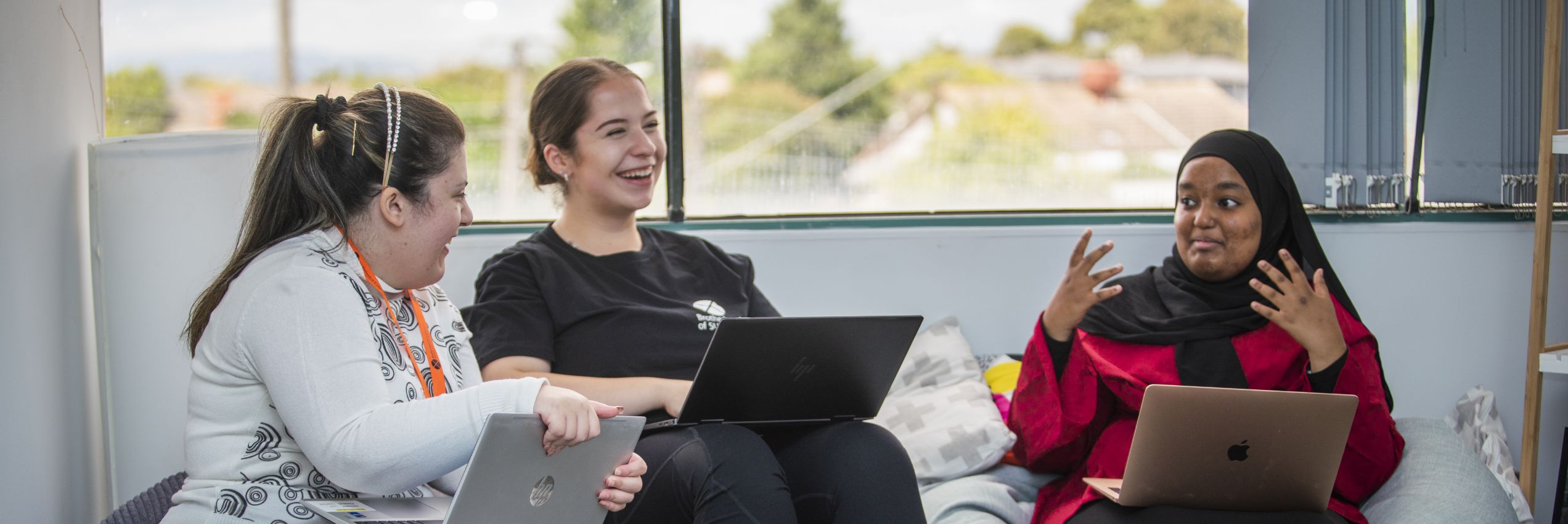BSL youth advisers Lina, Mary and Towheed sitting on a couch having a discussion, each with a laptop on their laps.