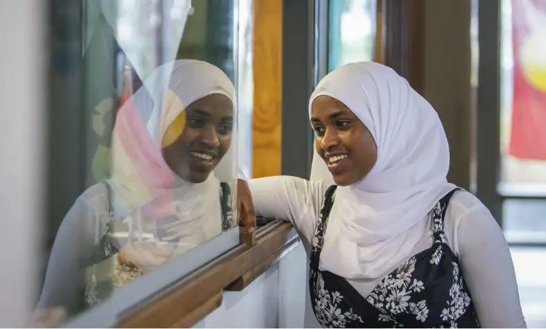 A dark-skinned person learning on a counter with their face reflected in the glass