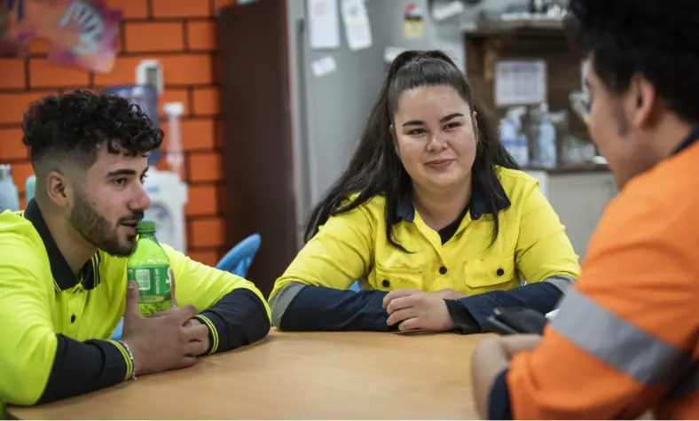 three people wearing hi-vis vests sitting at a lunch table having a discussion